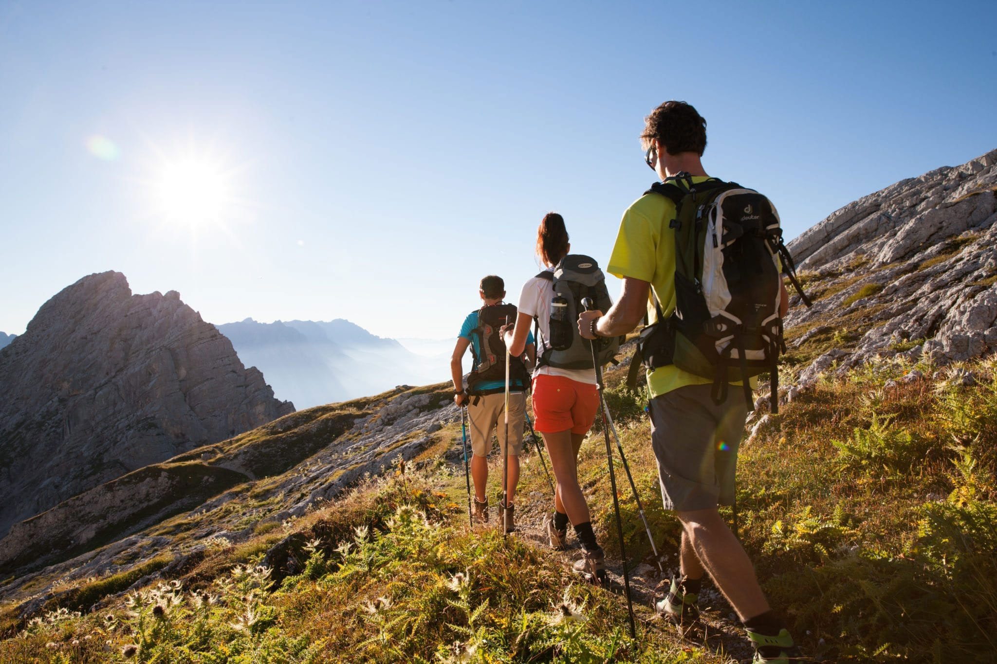 Immagine di un ragazzo e una ragazza, visti da lontano in cima una vetta di una montagna con il sole addosso. 